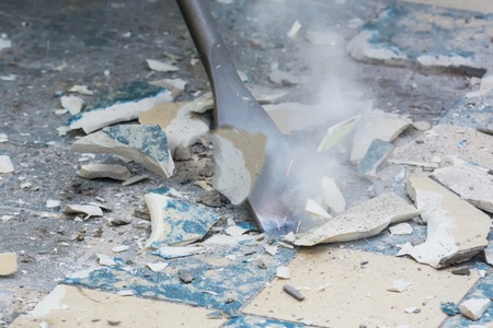 A tool being used to break tile on a floor and broken tile pieces